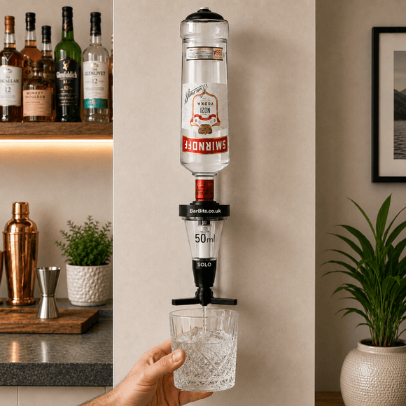 A wall-mounted bar spout made from an inverted Smirnoff vodka bottle, dispensing clear liquid into a glass held by a person's hand in a kitchen setting.
