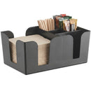 A black textured plastic multi-compartment bar caddy condiment and napkin dispenser, shown holding paper napkins, wooden stir sticks, and assorted tea bags on a white background.
