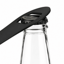 A black bar blade bottle opener tool resting on a clear glass bottle against a white background.