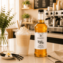 Bottle of Beaumont Vanilla syrup on a counter with a vanilla latte and vanilla beans.