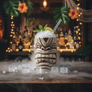 Tiki cocktail with ice and garnish in a decorative glass on a bar with a warm ambiance.