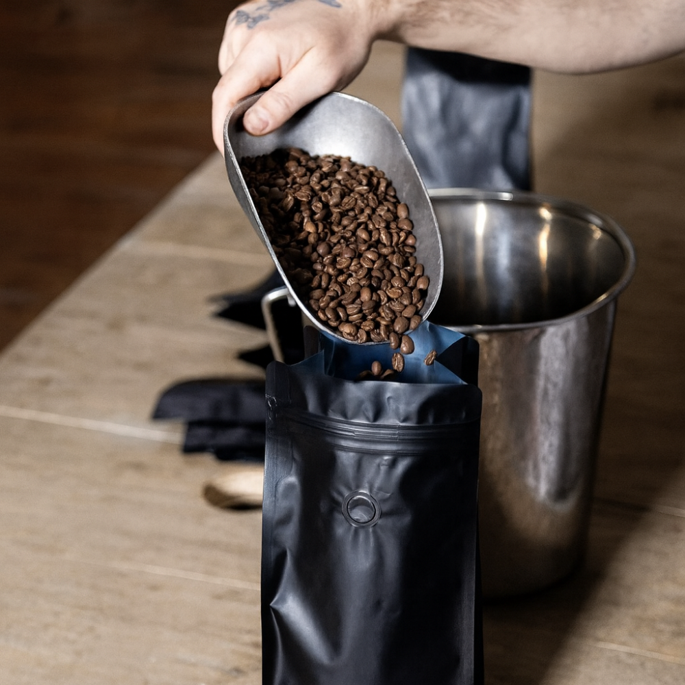 Person pouring coffee beans into a grinder on a wooden surface