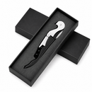 A black and silver corkscrew tool presented in an open black gift box with two additional closed boxes behind it on a white background.