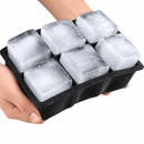 A hand holding a black silicone mold filled with six large, textured ice cubes against a plain white background.