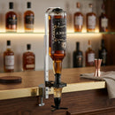 A bottle of whisky suspended upside down in a metal bar dispenser mounted on a wooden bar counter, with blurred liquor bottles in the background.