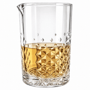 A clear glass mixing tumbler with a pouring spout, partially filled with amber liquid, shown on a clean white background.