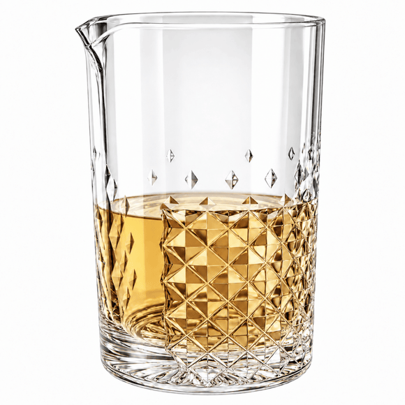 A clear glass mixing tumbler with a pouring spout, partially filled with amber liquid, shown on a clean white background.
