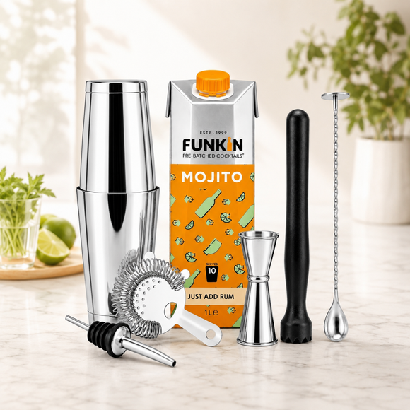 A cocktail mixing set arranged on a light marble countertop, including a stainless steel shaker, orange Funkin Mojito carton, jigger, muddler, strainer, and bar spoon, with lime and herbs in the background.