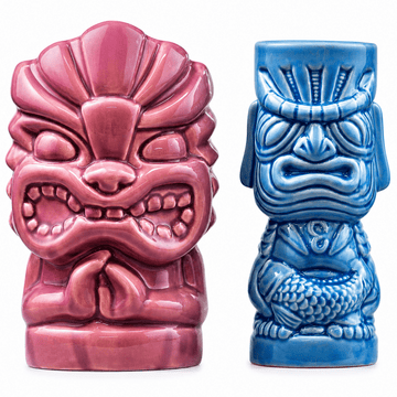 Two ceramic tiki-style mug or cup figurines on a white background: one in glossy pink and one in glossy blue, both with carved facial features and textured bodies.