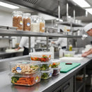 Prepared meals in containers on a kitchen counter with chefs in the background