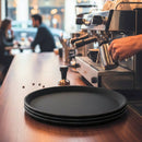 Barista preparing coffee at a counter with black trays in the foreground