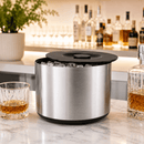 Metallic ice bucket on a marble surface with glasses of whiskey and bottles in the background.