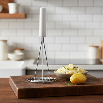 Masher on a wooden cutting board with mashed potatoes and a bowl in a kitchen setting