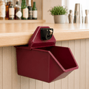 A dark red wall-mounted dispenser with a black dial and gold handle, mounted on a light wood bar counter in a bar setting.