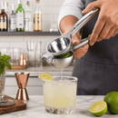 Person using a manual juicer to extract juice from a lime over a glass with a cocktail.