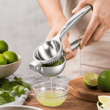 Person using a manual lime squeezer to extract juice into a small glass bowl on a wooden surface.